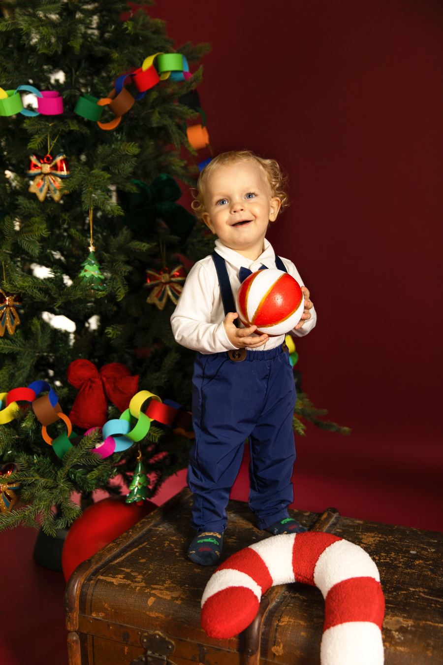 Weihnachtsfoto im Studio: Kind vor rotem Hintergrund mit Tannenbaum