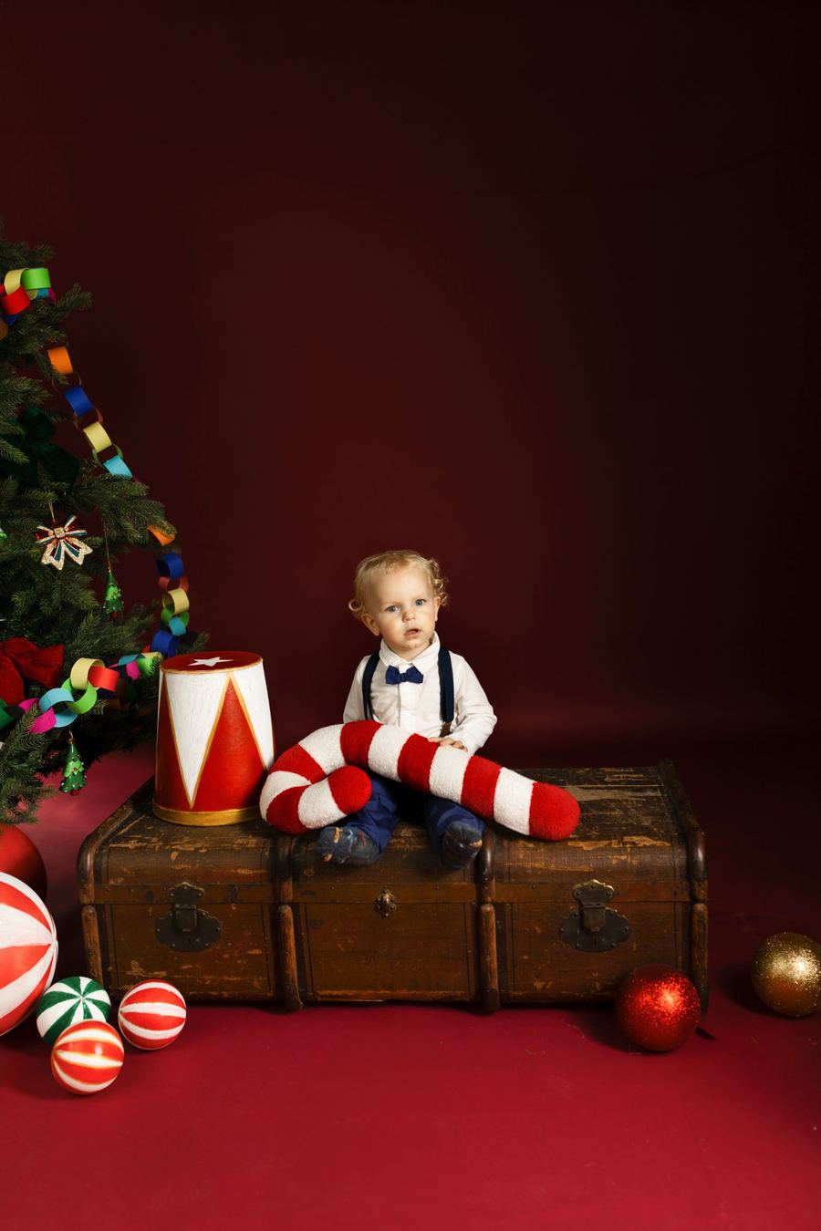 Weihnachtsfoto im Studio: Kind vor rotem Hintergrund mit Tannenbaum