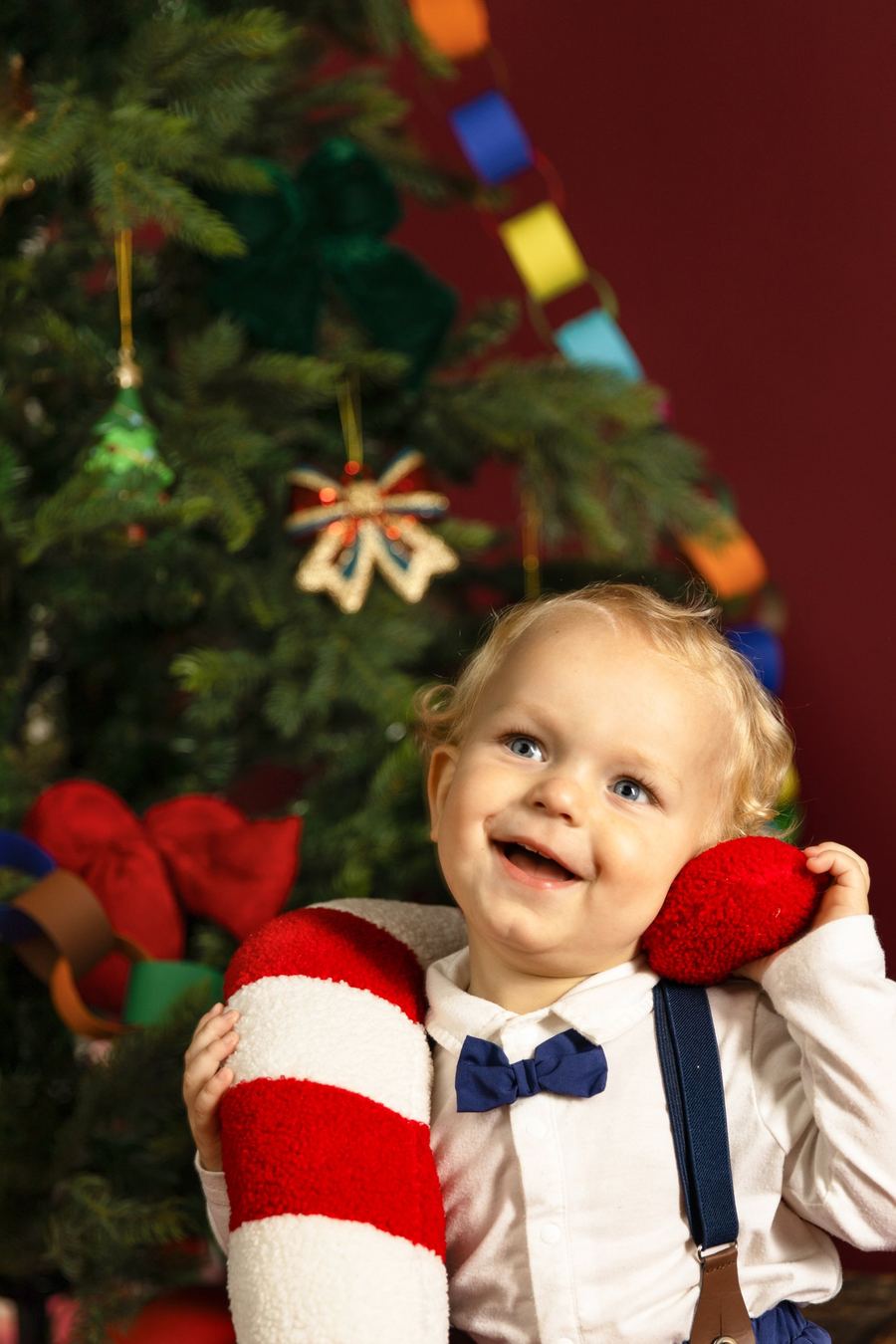 Weihnachtsfoto im Studio: Kind vor rotem Hintergrund mit Tannenbaum