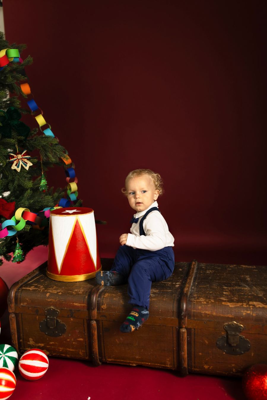 Weihnachtsfoto im Studio: Kind vor rotem Hintergrund mit Tannenbaum