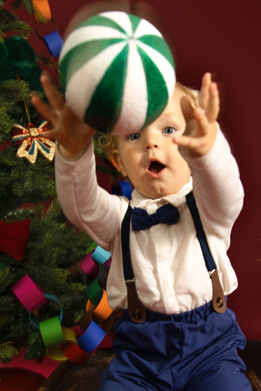 Weihnachtsfoto im Studio: Kind vor rotem Hintergrund mit Tannenbaum