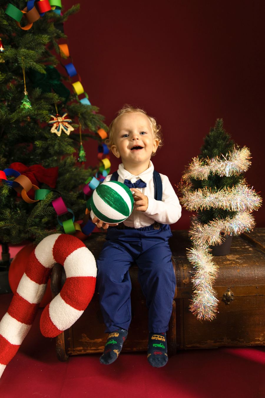 Weihnachtsfoto im Studio: Kind vor rotem Hintergrund mit Tannenbaum