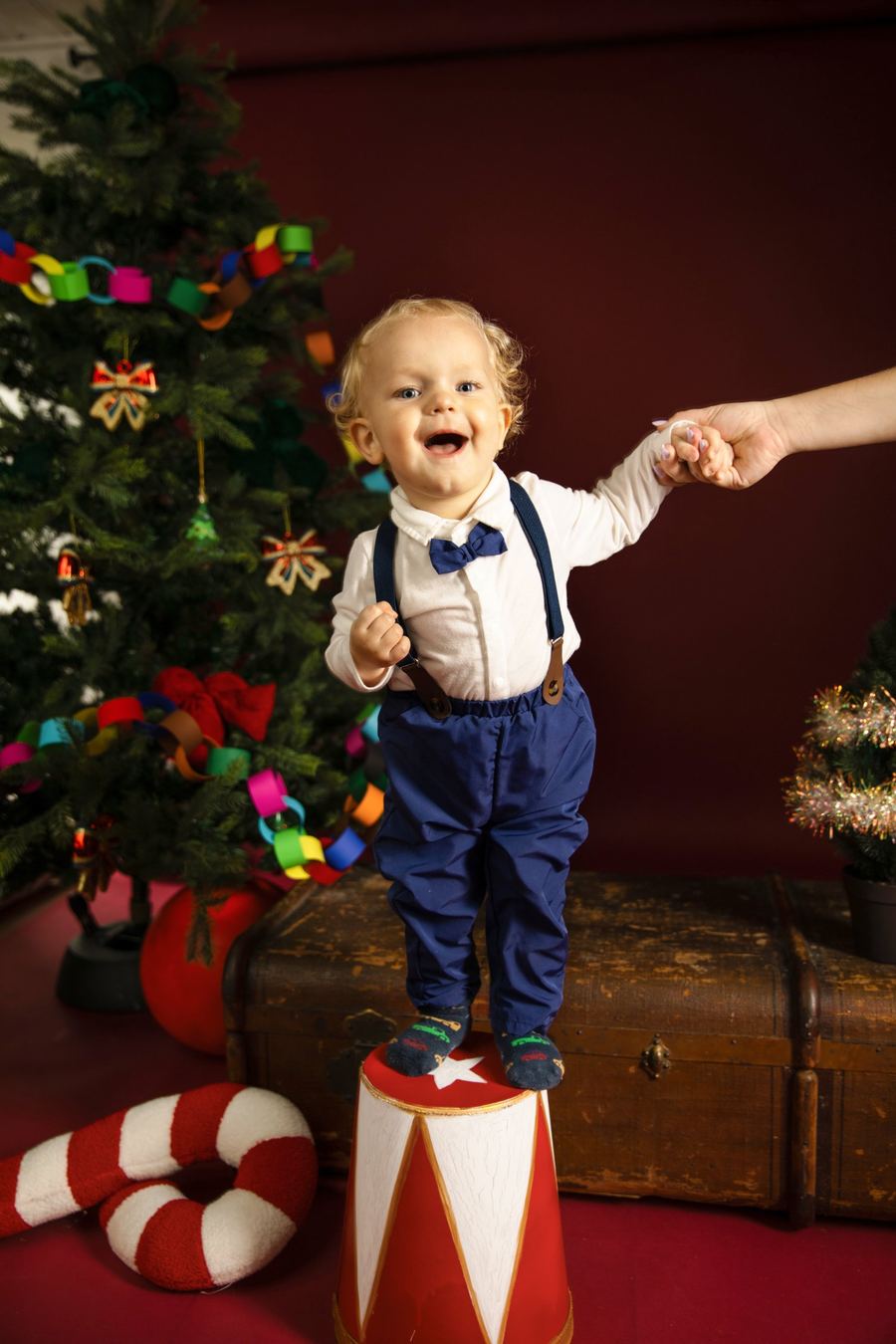 Weihnachtsfoto im Studio: Kind vor rotem Hintergrund mit Tannenbaum