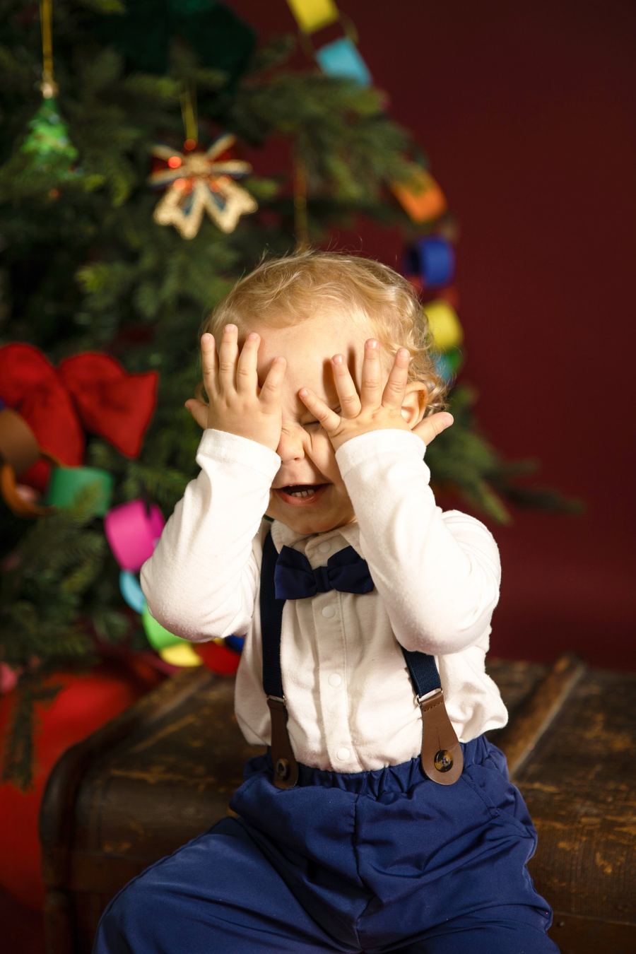 Weihnachtsfoto im Studio: Kind vor rotem Hintergrund mit Tannenbaum